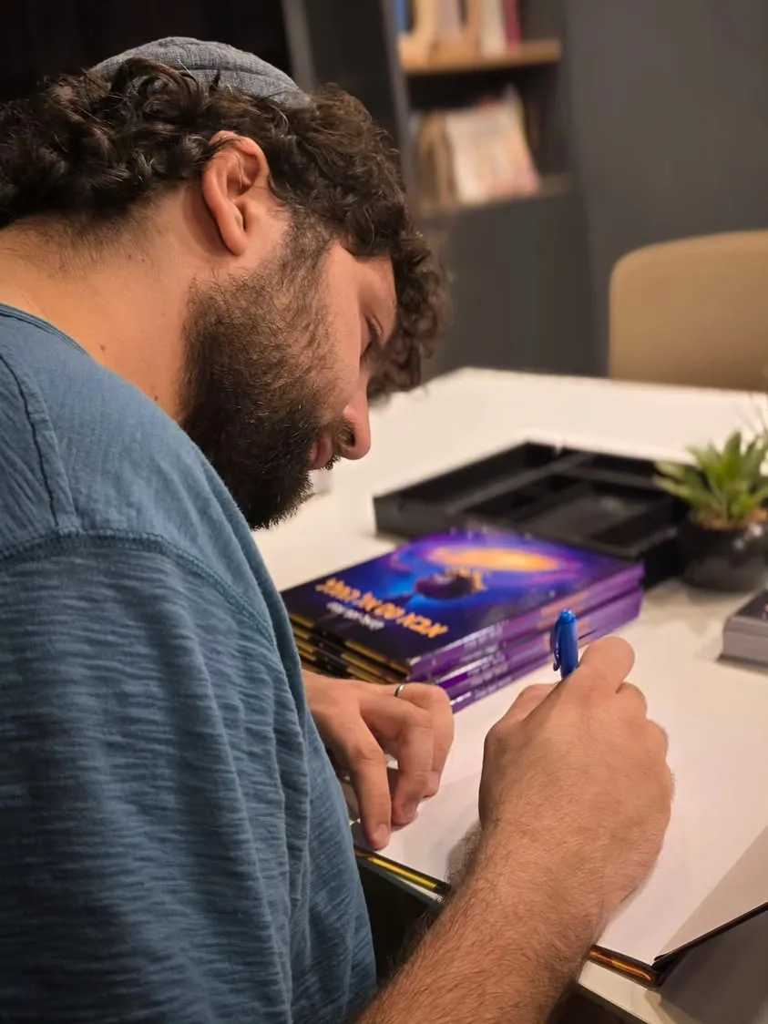 דניאל חותם בעט על עותק פתוח של הספר, וערימת ספרים לידו.